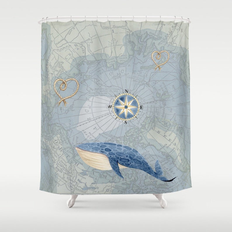 May include: A shower curtain featuring a vintage map design in shades of blue and gray. It includes a compass rose, rope heart accents, and a blue whale illustration. The nautical theme is prominent.