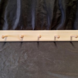 May include: A wooden wall-mounted coat rack with five knobs. The rack is made of natural wood and has a light brown color.
