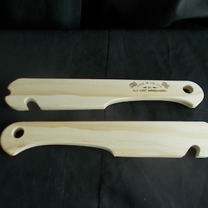 May include: Two light-colored wooden weaving tools with a curved handle and a notched end. The tools have a hole in the handle and the text "MADE IN THE USA BY OLD COOT WOODWORKS".