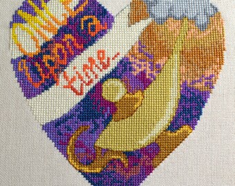 Op de afbeelding: Een paars, oranje en geel kruissteekhart met de tekst "Er was eens" in een banner bovenaan.