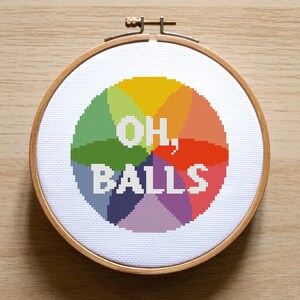 Peut inclure: Un cercle de broderie circulaire coloré avec la phrase "OH, BALLS" en lettres blanches.