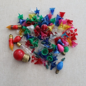 May include: A collection of colorful Christmas light bulbs with various shapes and sizes. The bulbs are mostly red, blue, green, and yellow, with some clear bulbs. The bulbs are arranged in a pile on a white surface.