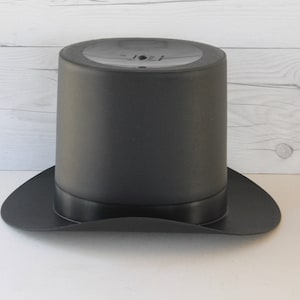 May include: A black top hat with a wide brim. The hat is made of a smooth, matte material.