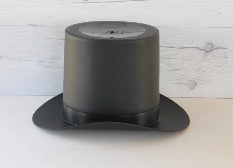 May include: A black top hat with a wide brim. The hat is made of a smooth, matte material.