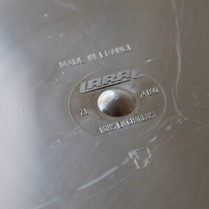 May include: Close-up of a silver metal disc with the text "MADE IN FRANCE" and "LARA L 74.690" printed on it. The disc also has the text "Z1" and "BOIS EN CHARBON" printed on it.