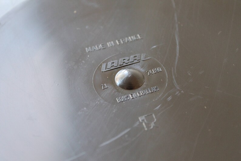 May include: Close-up of a silver metal disc with the text "MADE IN FRANCE" and "LARA L 74.690" printed on it. The disc also has the text "Z1" and "BOIS EN CHARBON" printed on it.