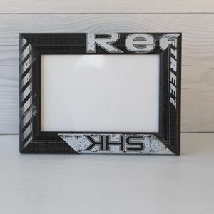 May include: Black picture frame with a white background. The frame has a hockey stick design with the words "Reebok" and "SHK" printed on it.