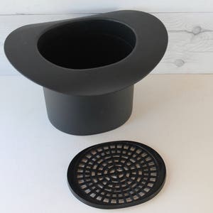 May include: Black plastic planter shaped like a top hat with a removable black plastic drainage disc.