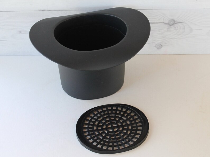 May include: Black plastic planter shaped like a top hat with a removable black plastic drainage disc.