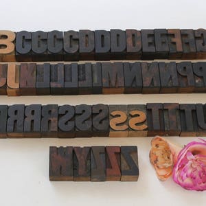 May include: A set of vintage wooden letterpress blocks in various sizes, including the letters A through Z. The blocks are arranged in rows, with some letters missing. The blocks are made of dark wood and have a worn, antique look.