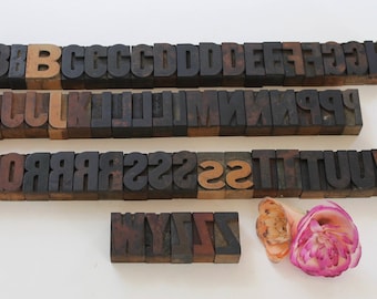 May include: A set of vintage wooden letterpress blocks in various sizes, including the letters A through Z. The blocks are arranged in rows, with some letters missing. The blocks are made of dark wood and have a worn, antique look.