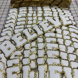 May include: A large pile of white felt patches with gold glitter trim, spelling out the word "BELIEVE".