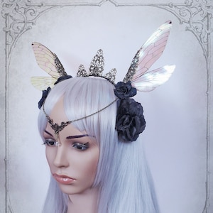 May include: A silver crown with black flowers and iridescent butterfly wings. The crown is adorned with intricate details and a delicate chain.