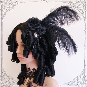 May include: A black wig with large curls styled in a vintage updo. The wig is adorned with a black feather and a black flower hairpiece with a cameo.