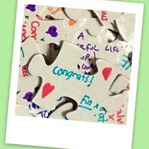 Puede incluir: Un rompecabezas blanco con las palabras "A Careful Life" y "Congrats!" escritas en &eacute;l. Las piezas del rompecabezas est&aacute;n decoradas con corazones y otros dibujos.