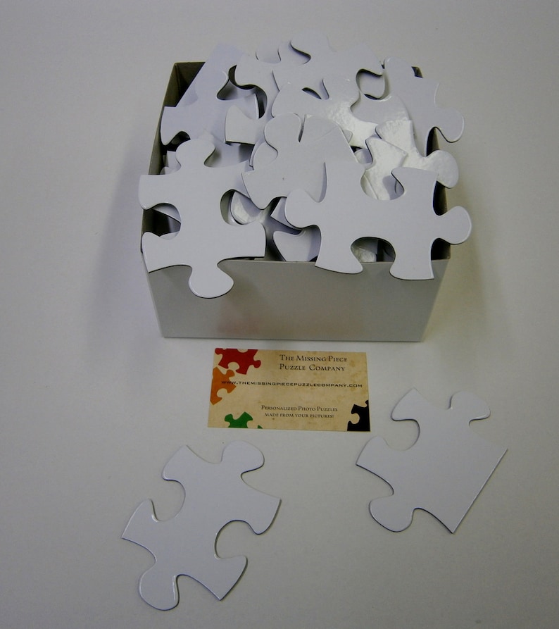 Puede incluir: Una caja blanca llena de piezas de rompecabezas blancas en blanco. La caja est&aacute; sentada sobre una superficie blanca. Una tarjeta de presentaci&oacute;n para "The Missing Piece Puzzle Company" est&aacute; en primer plano. La tarjeta tiene un dise&ntilde;o de rompecabezas colorido y el texto "Personalized Photo Puzzles Made from Your Pictures".