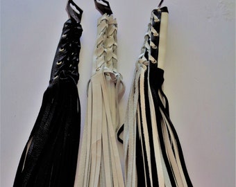 May include: Three leather whips with fringe. One is black, one is white, and one is black and white.