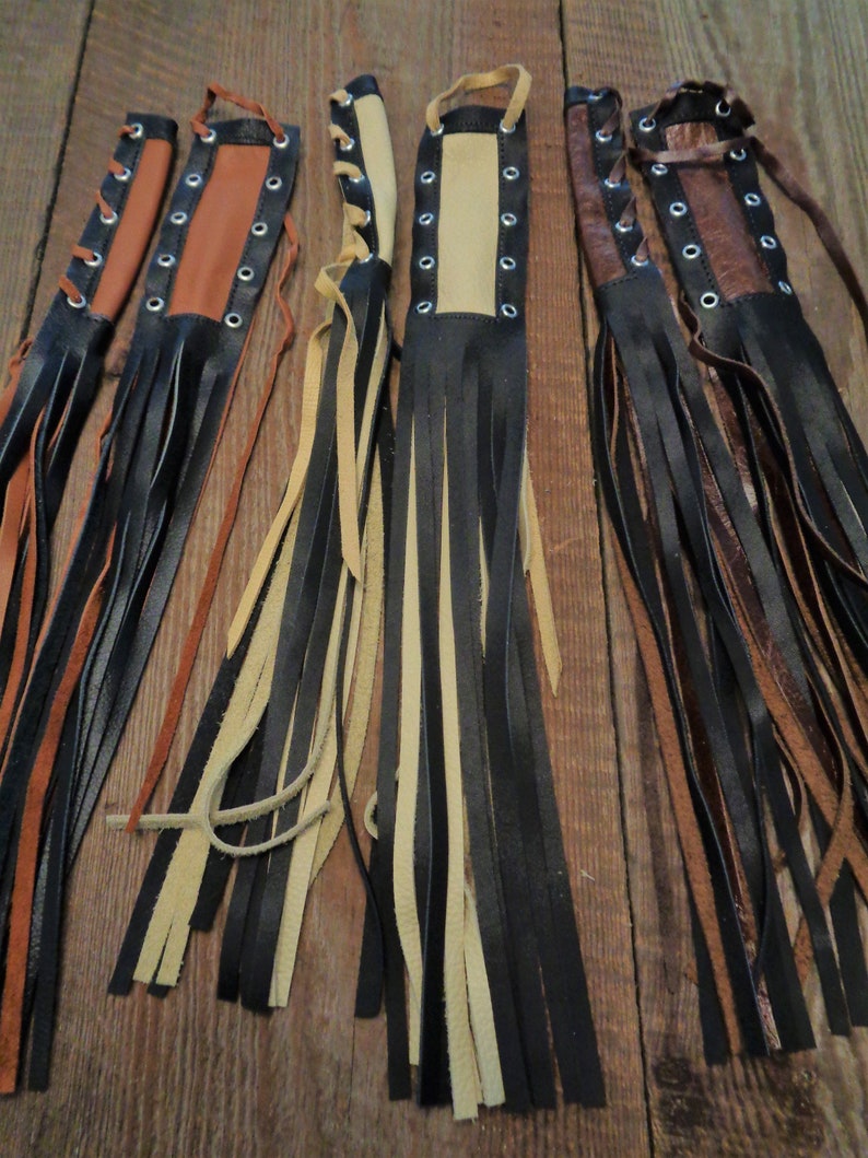 May include: Five leather tassels with black, brown, and beige leather straps and fringe. Each tassel has a row of silver eyelets and a lace-up closure.