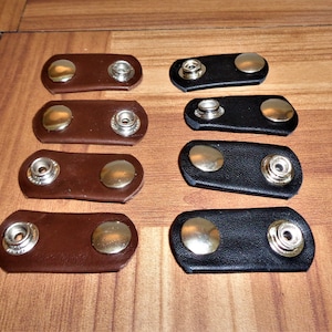 May include: Eight leather strap fasteners with metal snaps. Four are brown and four are black.