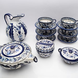 Peut inclure: Un service à thé en céramique bleu et blanc avec une théière, un pot à crème, un sucrier et quatre tasses et soucoupes. L'ensemble présente un motif floral avec des fleurs et des feuilles bleues sur un fond blanc.