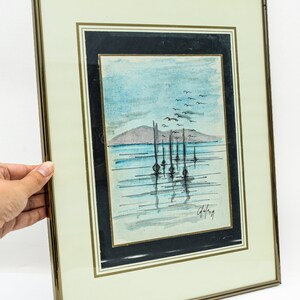 May include: A framed watercolor painting of a seascape with a row of boats in the water. The sky is blue and there are birds flying overhead. The painting is signed "Galang" in the bottom right corner.