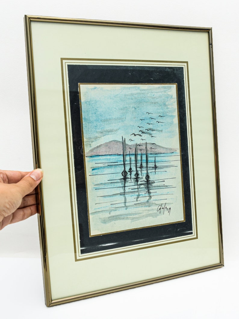 May include: A framed watercolor painting of a seascape with a row of boats in the water. The sky is blue and there are birds flying overhead. The painting is signed "Galang" in the bottom right corner.