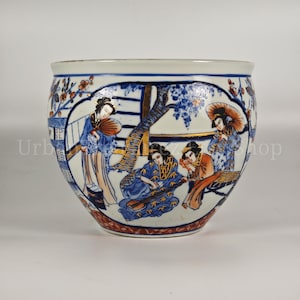 Könnte beinhalten: Eine große, runde Keramikschale mit einem detaillierten, handgemalten Design. Die Schale hat einen weißen Hintergrund mit blauen und goldenen Akzenten, die Figuren in traditioneller japanischer Kleidung darstellen. Der Rand ist weiß mit einem blauen Blumenmuster.