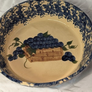 May include: A ceramic pie plate with a blue and white speckled rim and a hand-painted design of a basket of grapes.