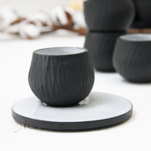 May include: A black ceramic cup with a white interior and a textured exterior. The cup is sitting on a white ceramic saucer with a black rim.