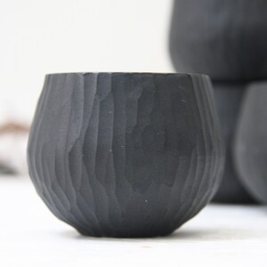 May include: Four black ceramic cups with a textured, wood-like finish. The cups are stacked on top of each other.