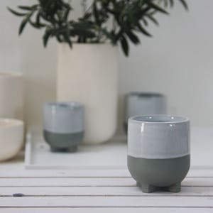Op de afbeelding: Een set van vier grijze en witte keramische bekers met een uniek ontwerp. Elke beker heeft een grijze basis en een witte bovenkant, wat een tweekleurig effect cre&euml;ert. De bekers zijn op een wit oppervlak gerangschikt.
