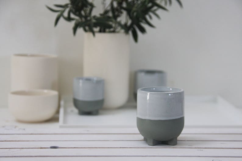 Op de afbeelding: Een set van vier grijze en witte keramische bekers met een uniek ontwerp. Elke beker heeft een grijze basis en een witte bovenkant, wat een tweekleurig effect cre&euml;ert. De bekers zijn op een wit oppervlak gerangschikt.