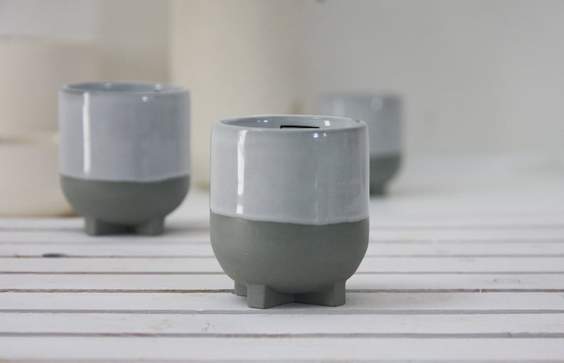 Op de afbeelding: Drie grijze keramische potten met een witte glazuur op de bovenste helft. De potten hebben een afgeronde vorm en drie kleine voetjes.