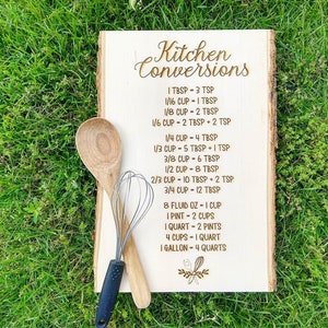 May include: A wooden sign with the words "Kitchen Conversions" written in a decorative font. The sign lists various kitchen conversions, such as tablespoons to teaspoons, cups to tablespoons, and pints to quarts.