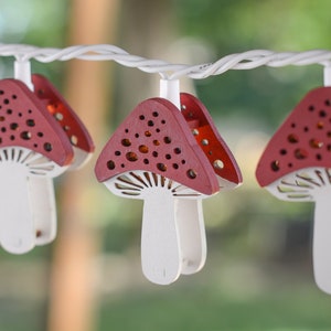 May include: A string of fairy lights with red and white mushroom-shaped lights. The lights are strung on a white wire and are hanging from a tree branch.