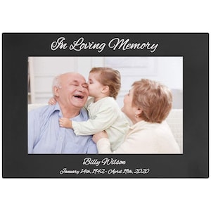 May include: Black picture frame with a photo of a family. The text "In Loving Memory" is at the top of the frame. The text "Billy Wilson" is below the photo. The dates "January 14th, 1942 - April 14th, 2020" are below the name.