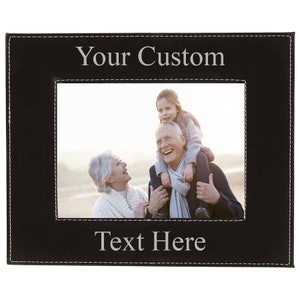 May include: Black leather photo frame with a stitched border. The frame has a white background with the text "Your Custom Text Here" in a silver font. The frame is holding a photo of a family of three.