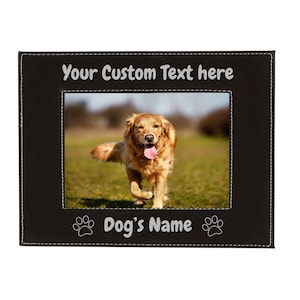 May include: Black leather photo frame with a stitched border. The frame has a cutout for a photo and a space for text. The text reads "Your Custom Text here" and "Dog's Name". A paw print graphic is on either side of the text. The photo shows a golden retriever running through a grassy field.