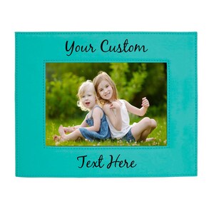 May include: A turquoise blue picture frame with a stitched border. The frame has a white mat and a photo of two young girls sitting on the grass. The text "Your Custom" is at the top of the frame and "Text Here" is at the bottom.