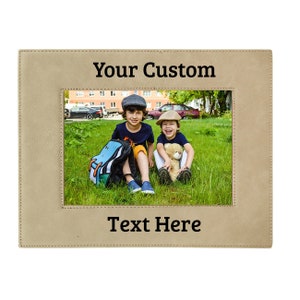 May include: Tan leather picture frame with a stitched border. The frame has a photo of two boys sitting on the grass. The text "Your Custom Text Here" is printed on the frame.