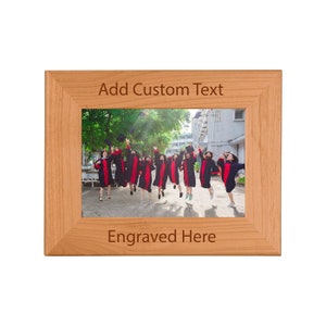 May include: A wooden picture frame with a photo of a group of people in graduation gowns jumping in the air. The frame has the text "Add Custom Text" and "Engraved Here" on it.