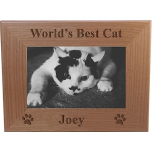 May include: A wooden picture frame with the text "World's Best Cat" and "Joey" engraved on it. The frame holds a black and white photo of a cat with black and white markings. Paw prints are engraved on the frame.