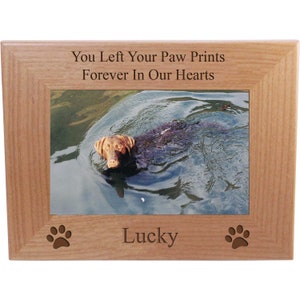 May include: A wooden picture frame with a photo of a brown dog swimming in a lake. The frame has the text "You Left Your Paw Prints Forever In Our Hearts" and "Lucky" engraved on it.
