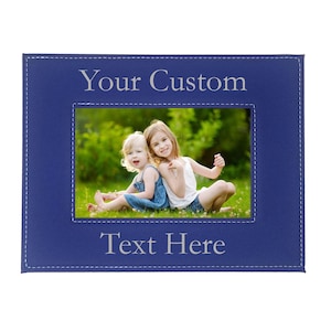 May include: A blue leather picture frame with a stitched border. The frame has a photo of two girls sitting on the grass. The text "Your Custom Text Here" is engraved on the frame.