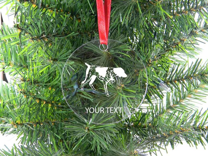 May include: Clear, round Christmas ornament with a white and black dog silhouette. The ornament hangs from a red ribbon and has the text "YOUR TEXT" at the bottom. The ornament is displayed against a backdrop of green Christmas tree branches.