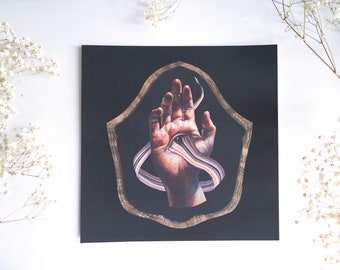 May include: A hand with a colorful ribbon wrapped around it, set against a black background with a gold frame.