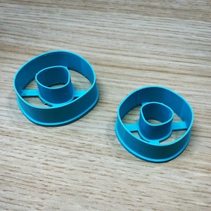 Puede incluir: Dos cortadores de rosquillas de plástico azul, uno más grande que el otro, sobre una superficie de madera.