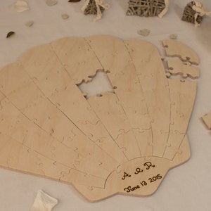 Puede incluir: Un rompecabezas de libro de visitas de madera con forma de concha de mar con el texto "A & R June 13, 2015" grabado en la parte inferior.