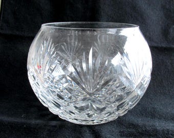 May include: A clear, round glass bowl featuring intricate cut-glass patterns. The exterior surface displays a combination of fan-shaped motifs and a diamond-cut crosshatch design that reflects light across the curved body of the vessel.