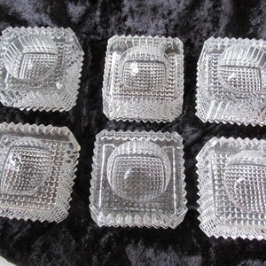 May include: Six clear glass square-shaped bowls with a textured, diamond-like pattern. The bowls are empty and have a slightly raised center.